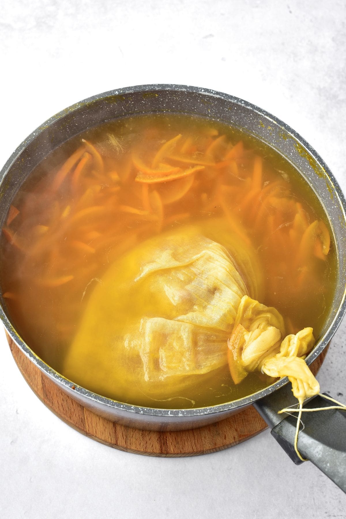 A muslin bag in a pot with orange peel slices and water
