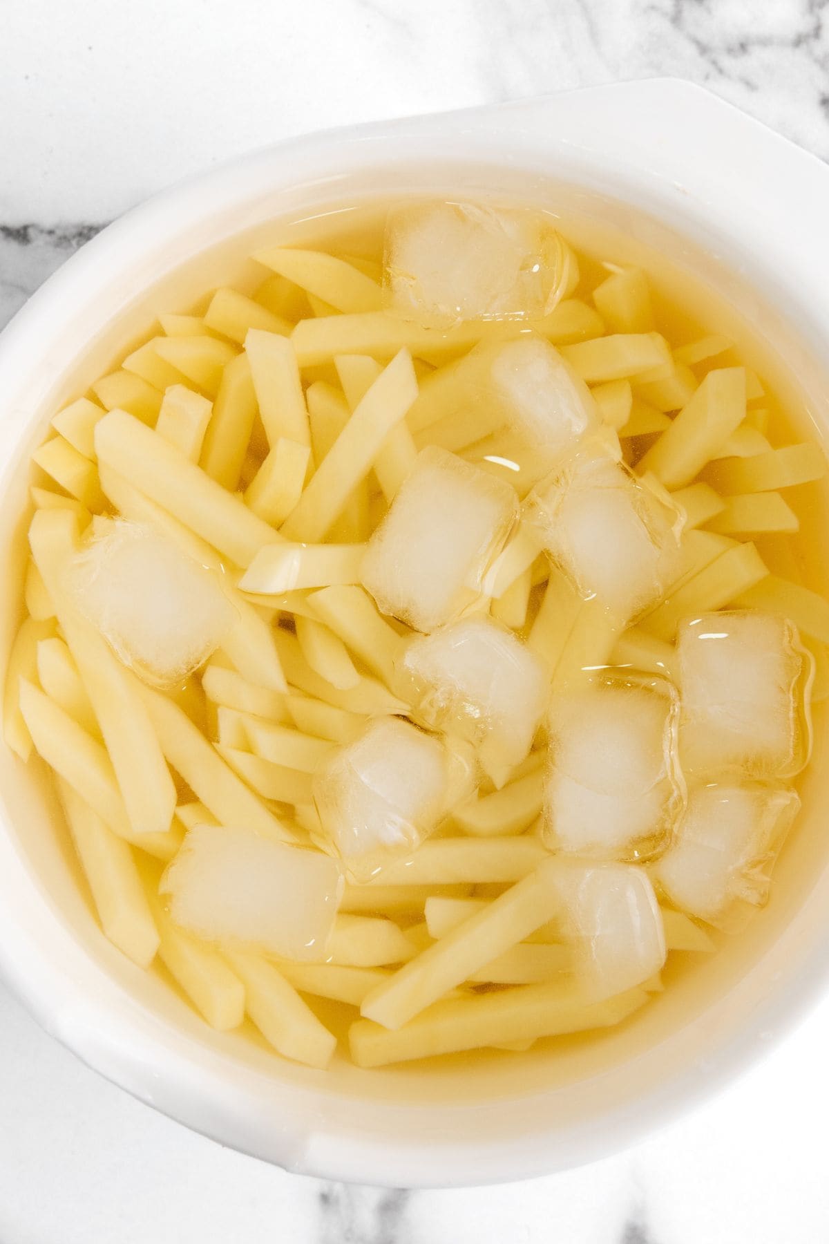 Raw cut fries in a bowl of ice water