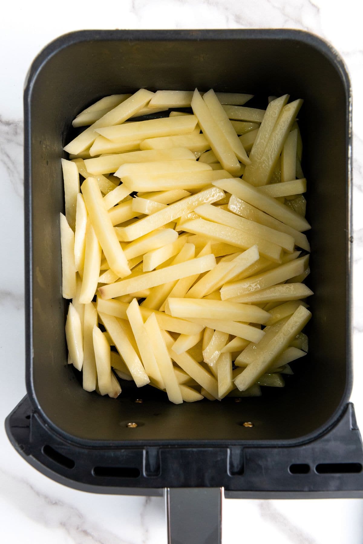 Fries tossed in oil in air fryer basket