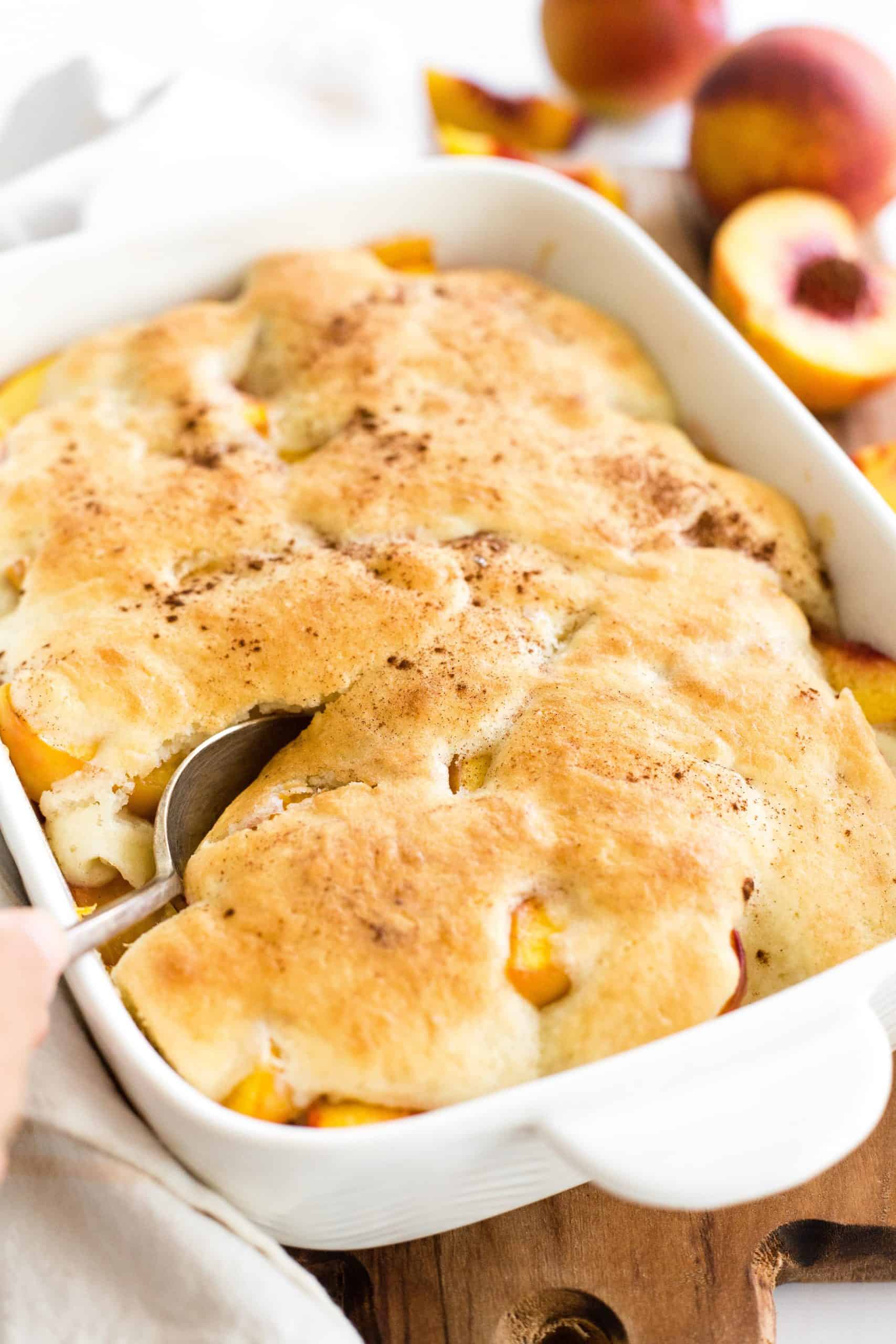Hand holding a spoon in a gluten-free peach cobbler.