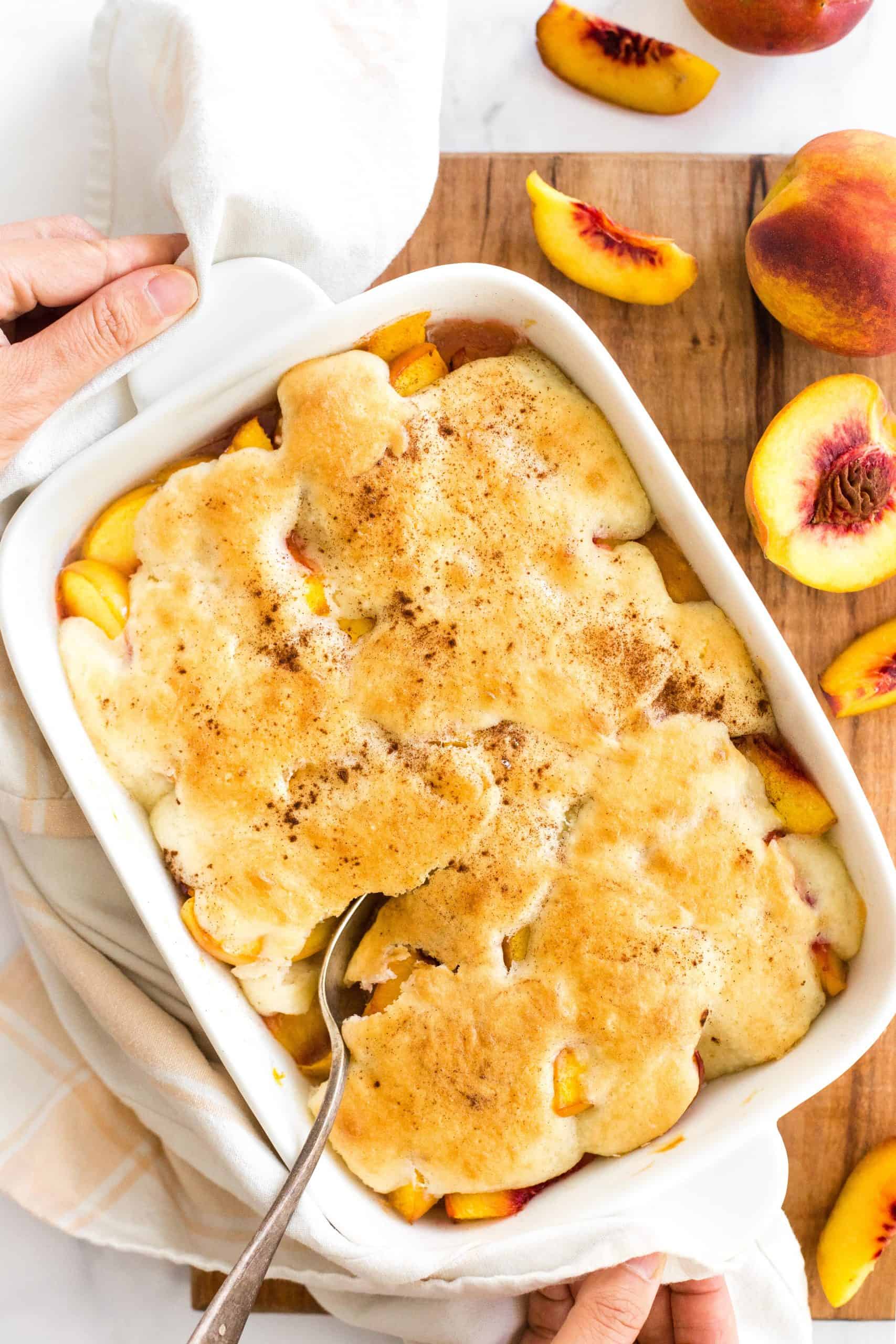 Two hands reaching for a cobbler-filled baking dish.
