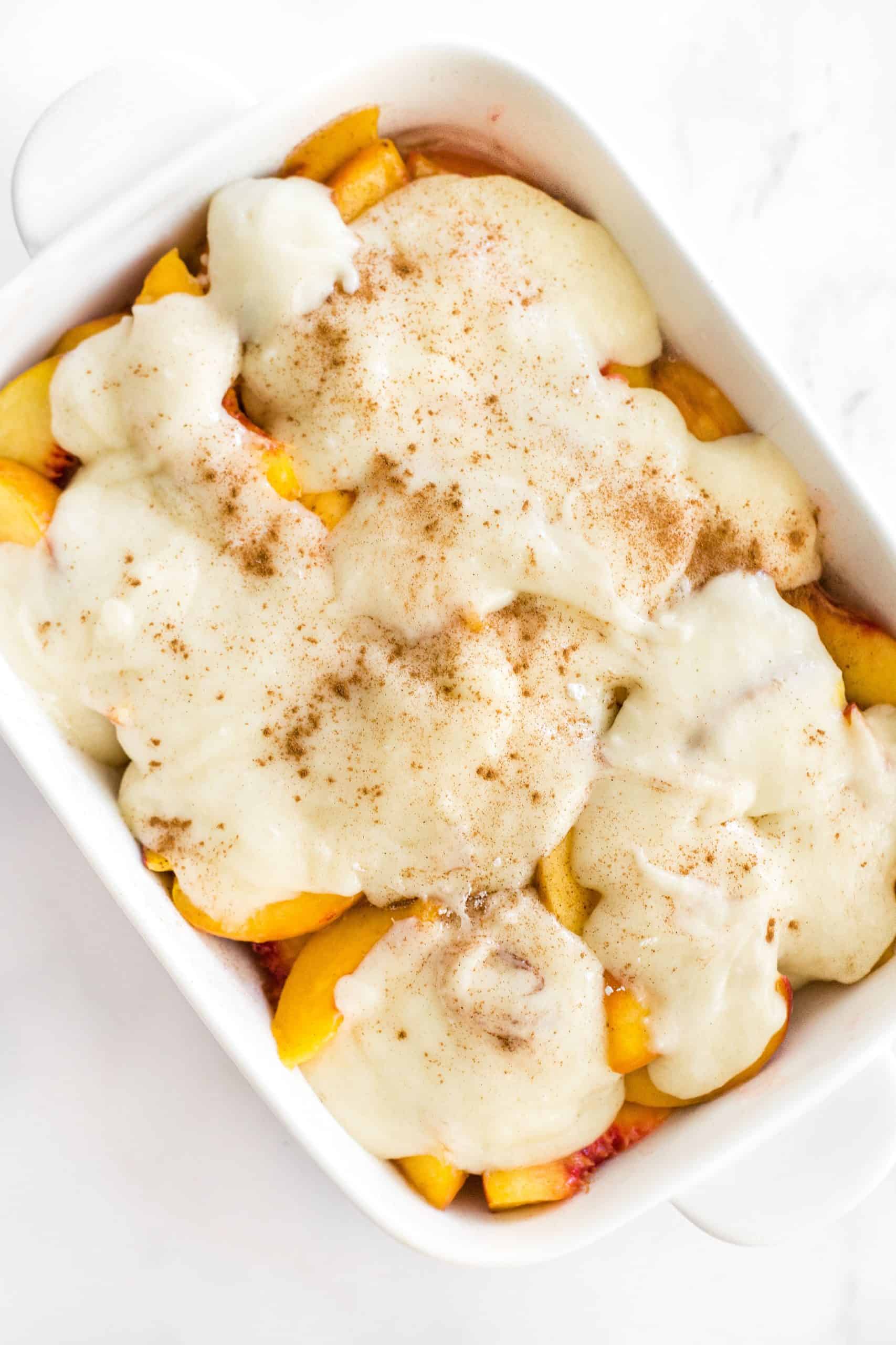 Cobbler topping on top of peach slices in a baking dish.