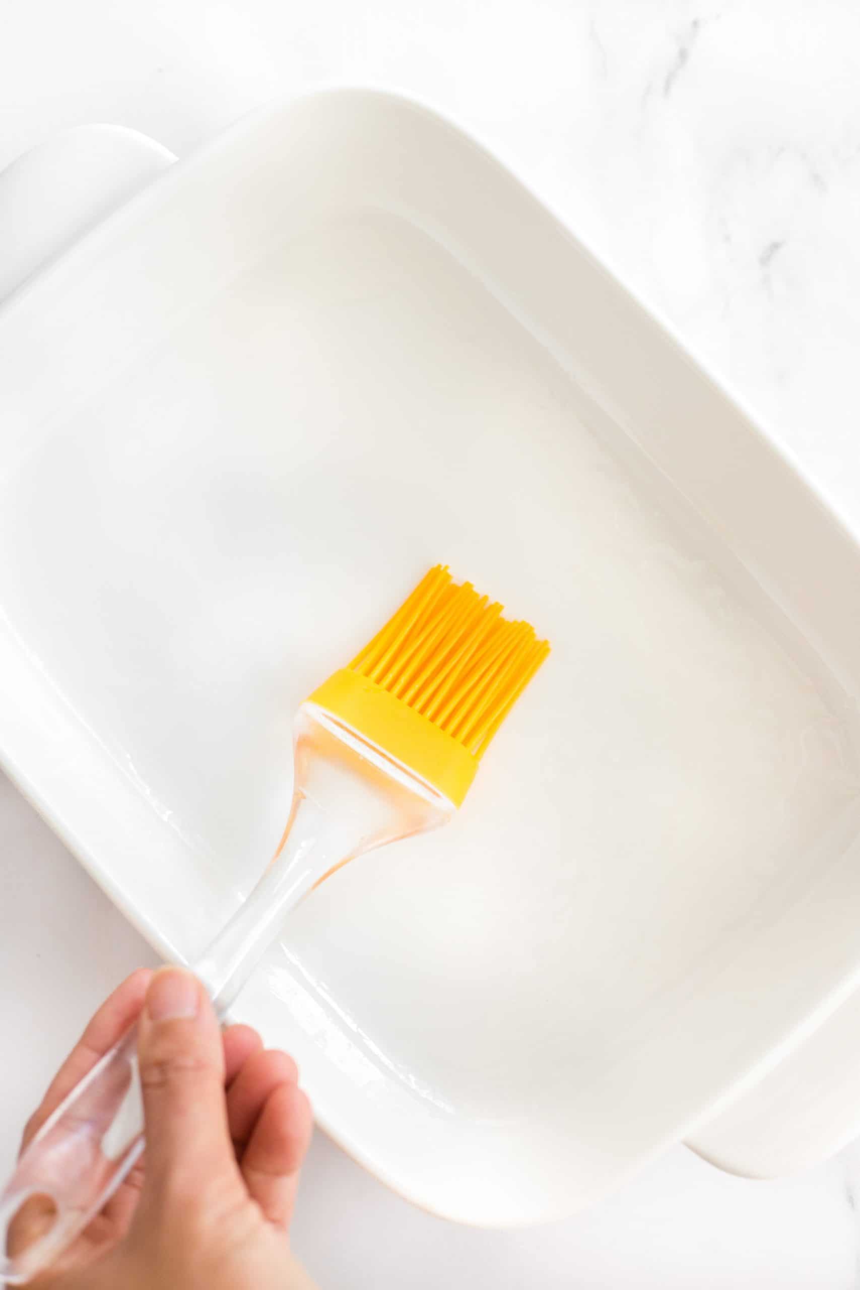 Brushing a white baking dish with oil.