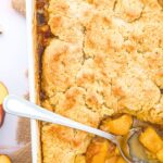 Top down view of half-eaten peach cobbler in casserole dish.