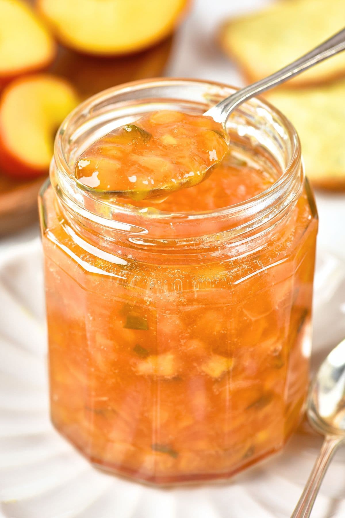 How to Make Peach Jalapeno Pepper Jam Holding up a spoonful of peach jalapeno jam from a jar