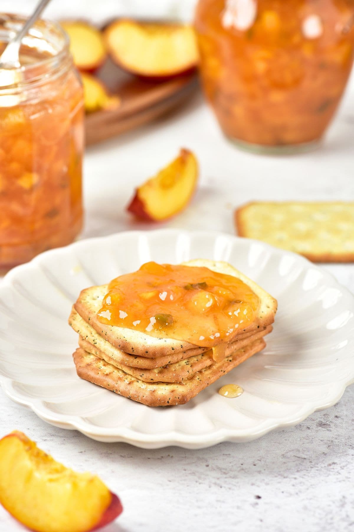 Spicy peach jam spread on a stack of crackers on plate.