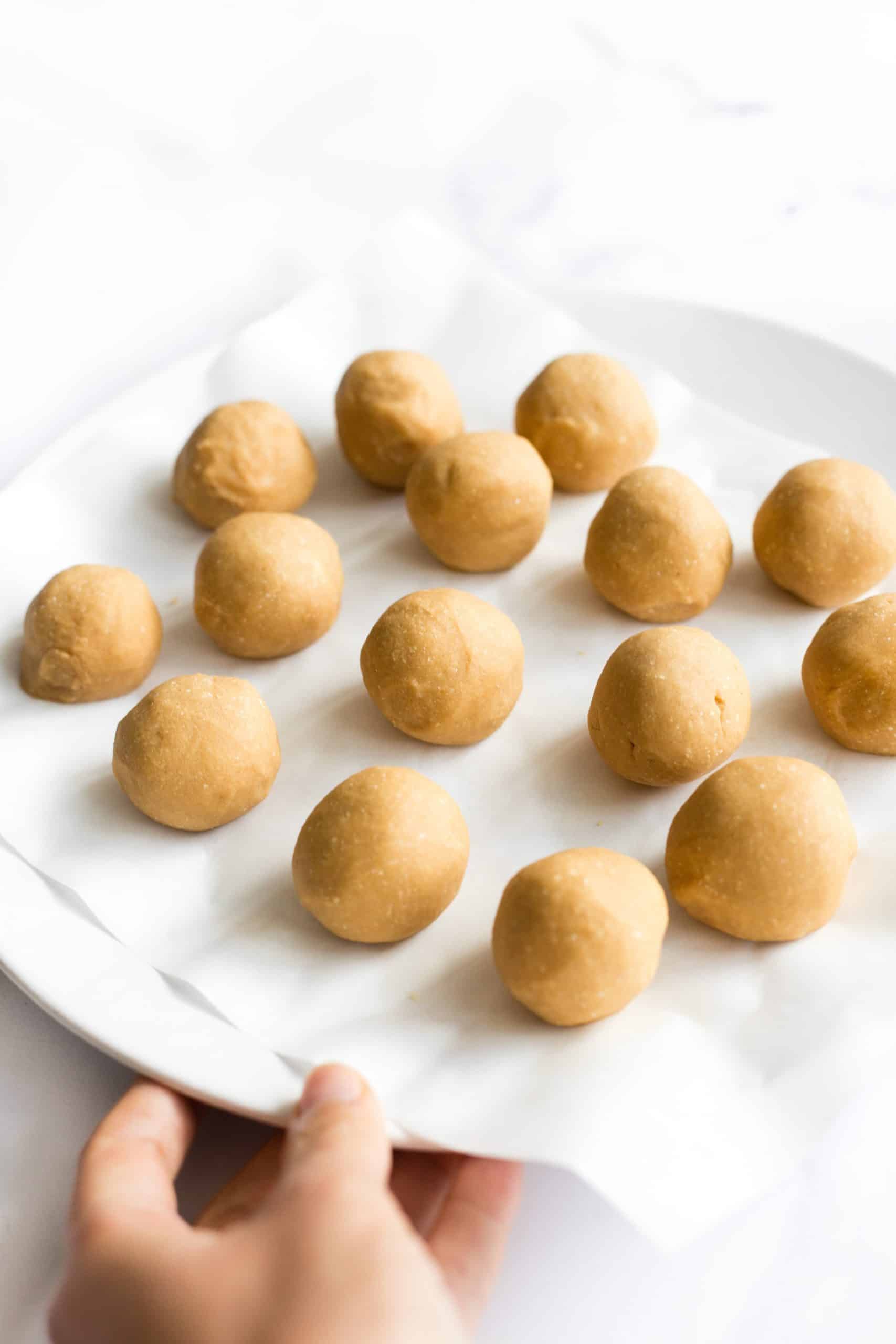 Hand holding a plate full of no-bake gluten-free peanut butter balls.