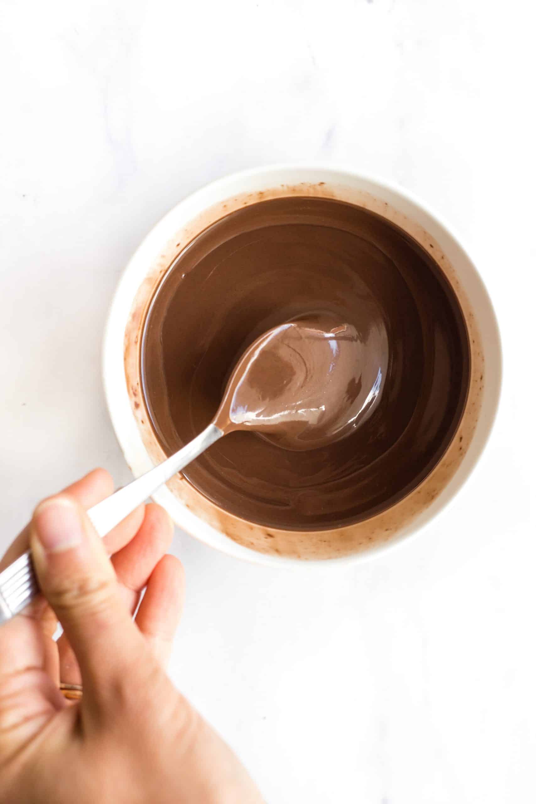 Using a spoon to stir melted chocolate in a small white bowl.
