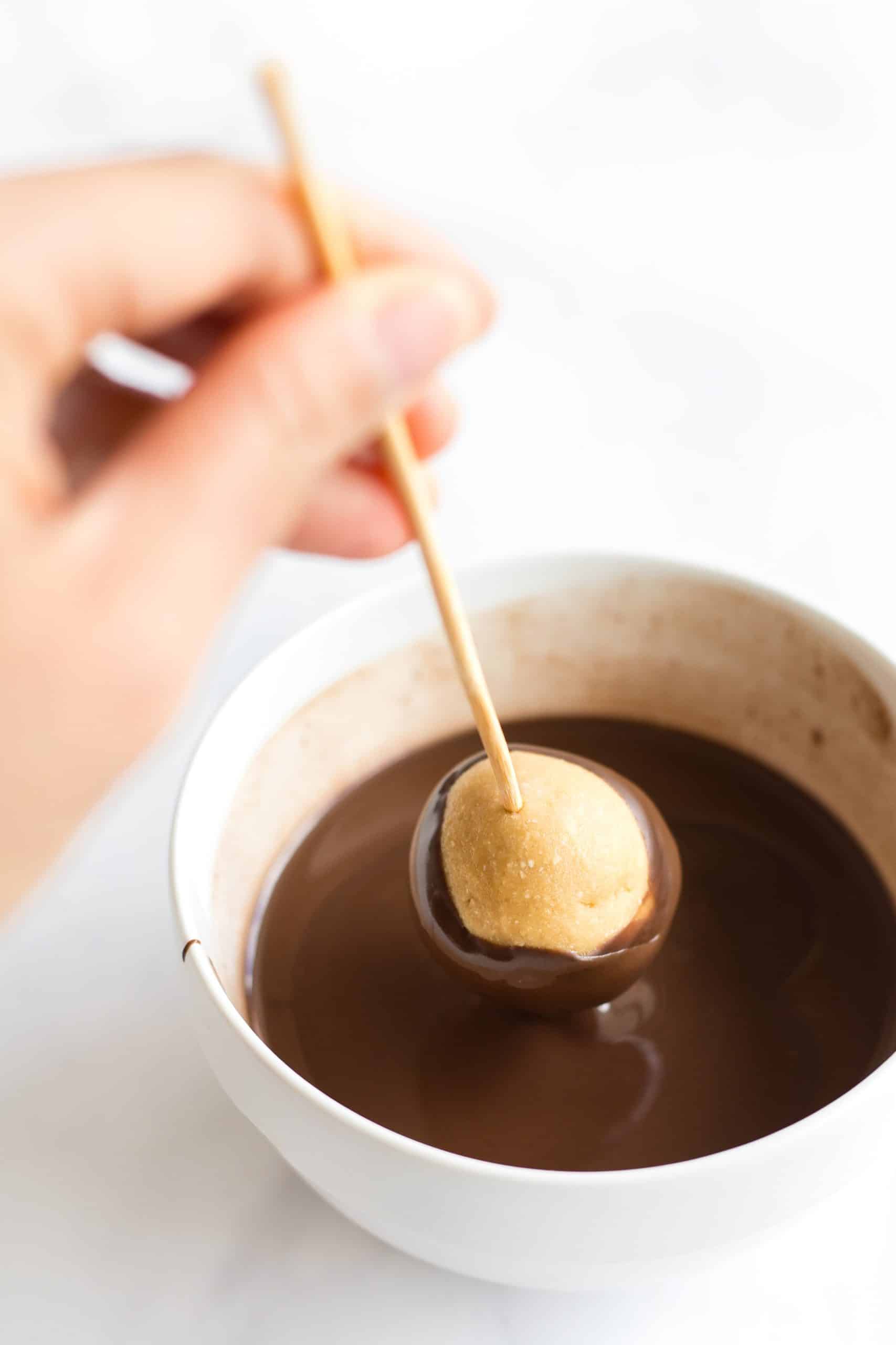 Using a stick to dip a peanut butter ball in melted chocolate.