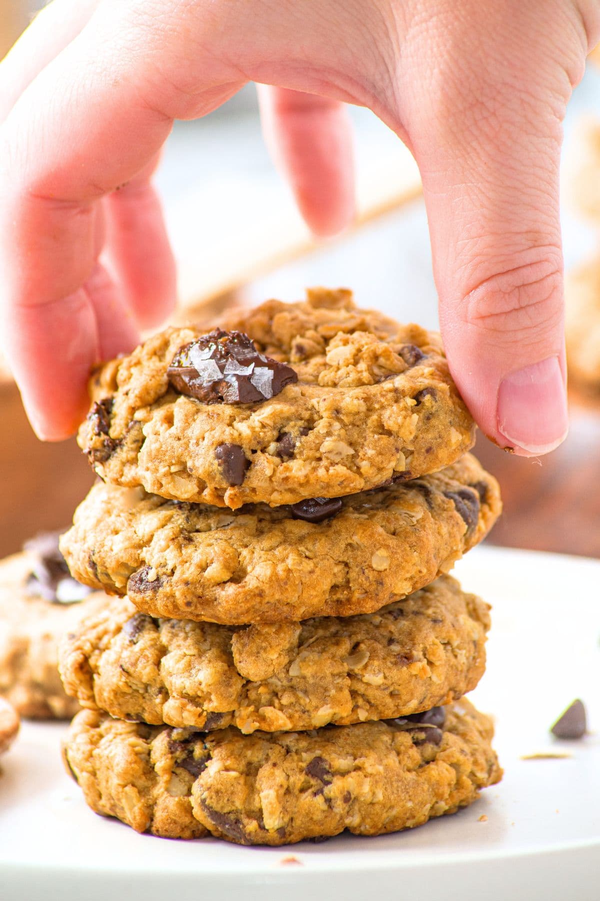 Hand picking up a chocolate chip oatmeal cookie from a stack