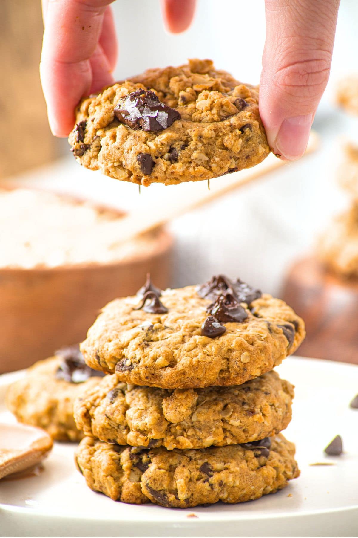 Holding up a peanut butter oatmeal chocolate chip cookie from a stack of cookies.
