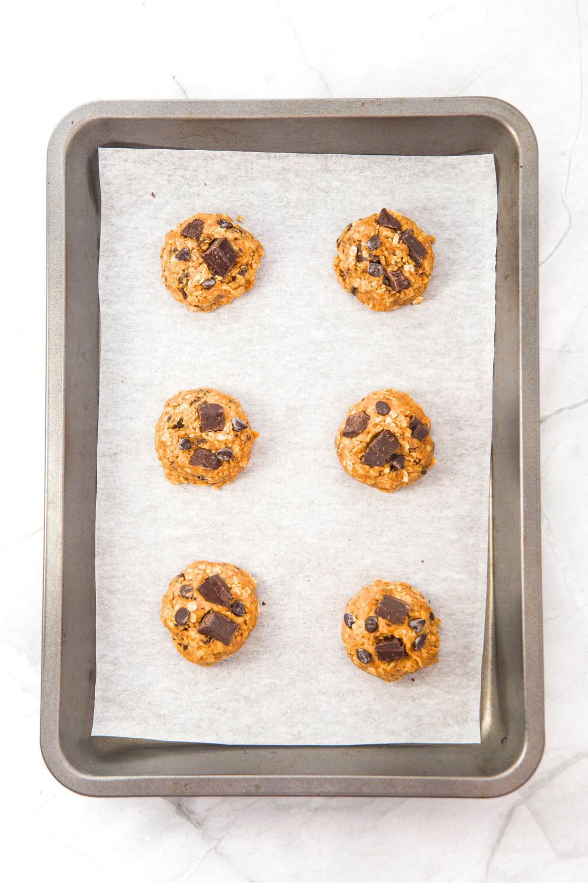 Cookie dough balls on parchment-lined baking sheet.