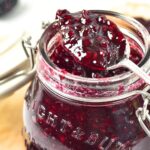 Holding a spoonful of blackberry jam from a jar