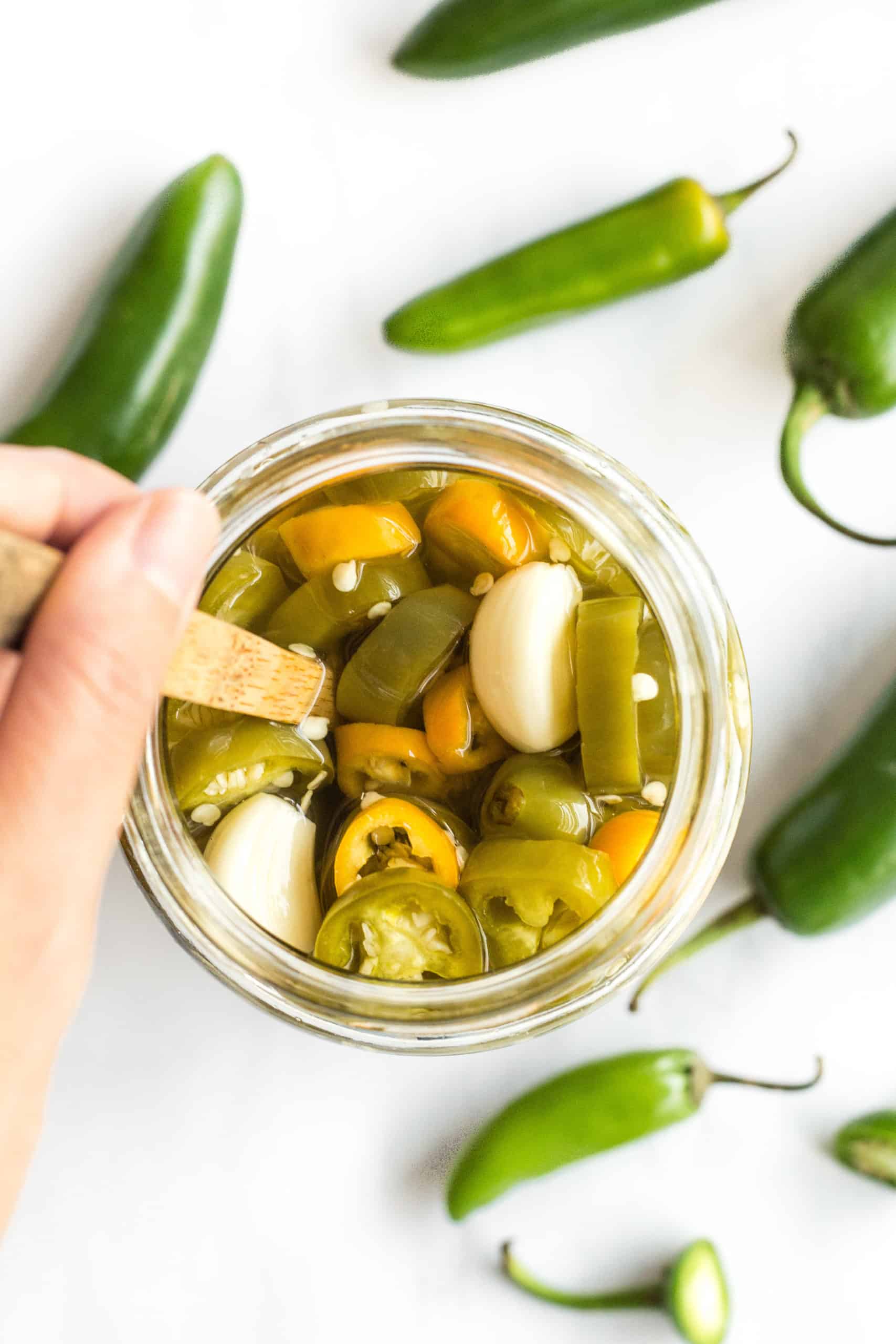 Hand stirring a jar of pickled jalapeño peppers.