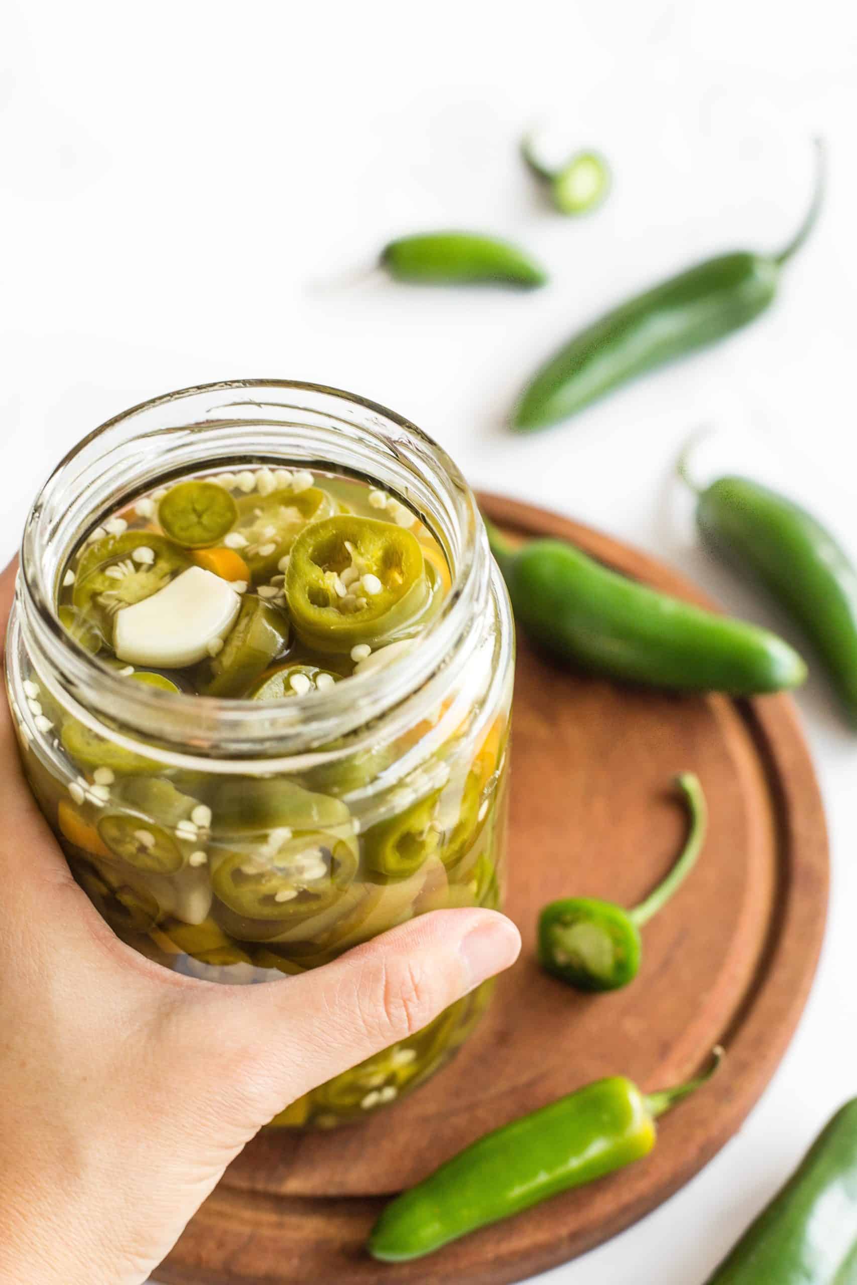 Hand holding a jar of jalapeño pickles.