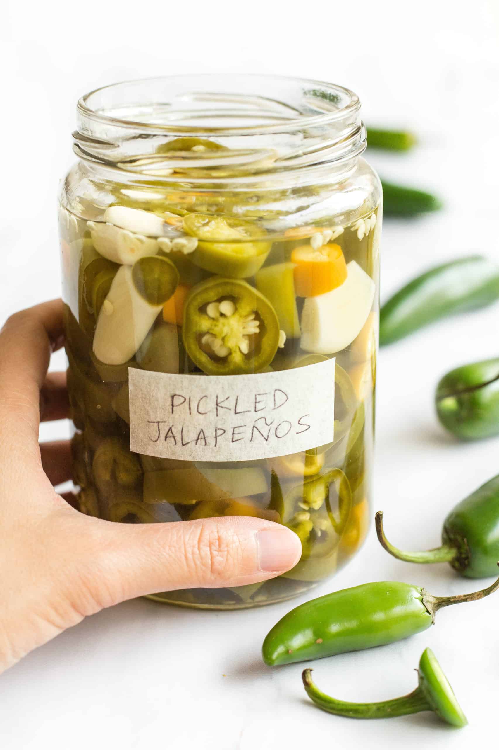Hand holding a jar of freshly pickled jalapeño peppers.