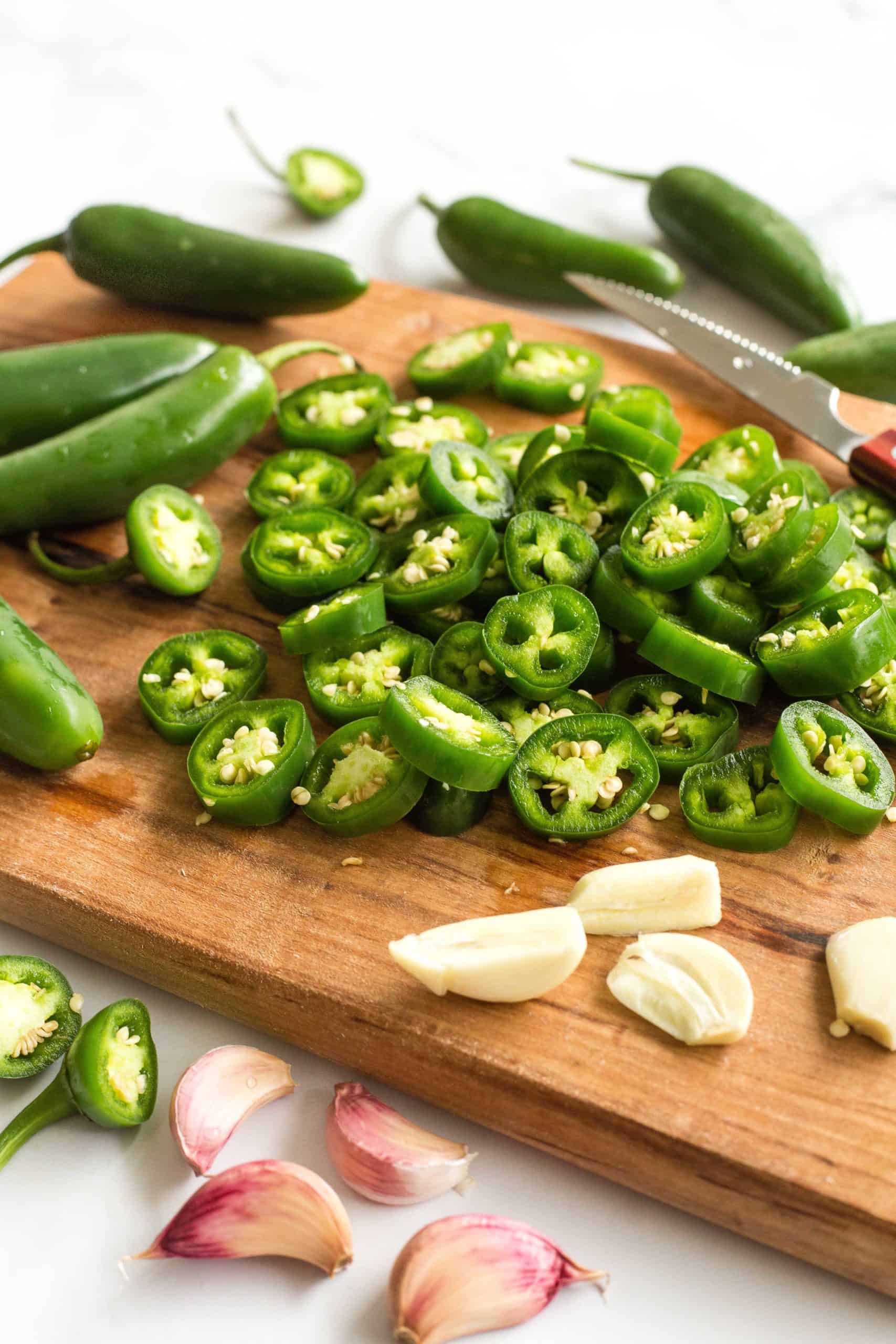 Sliced jalapeno peppers and garlic cloves on a wooden board.