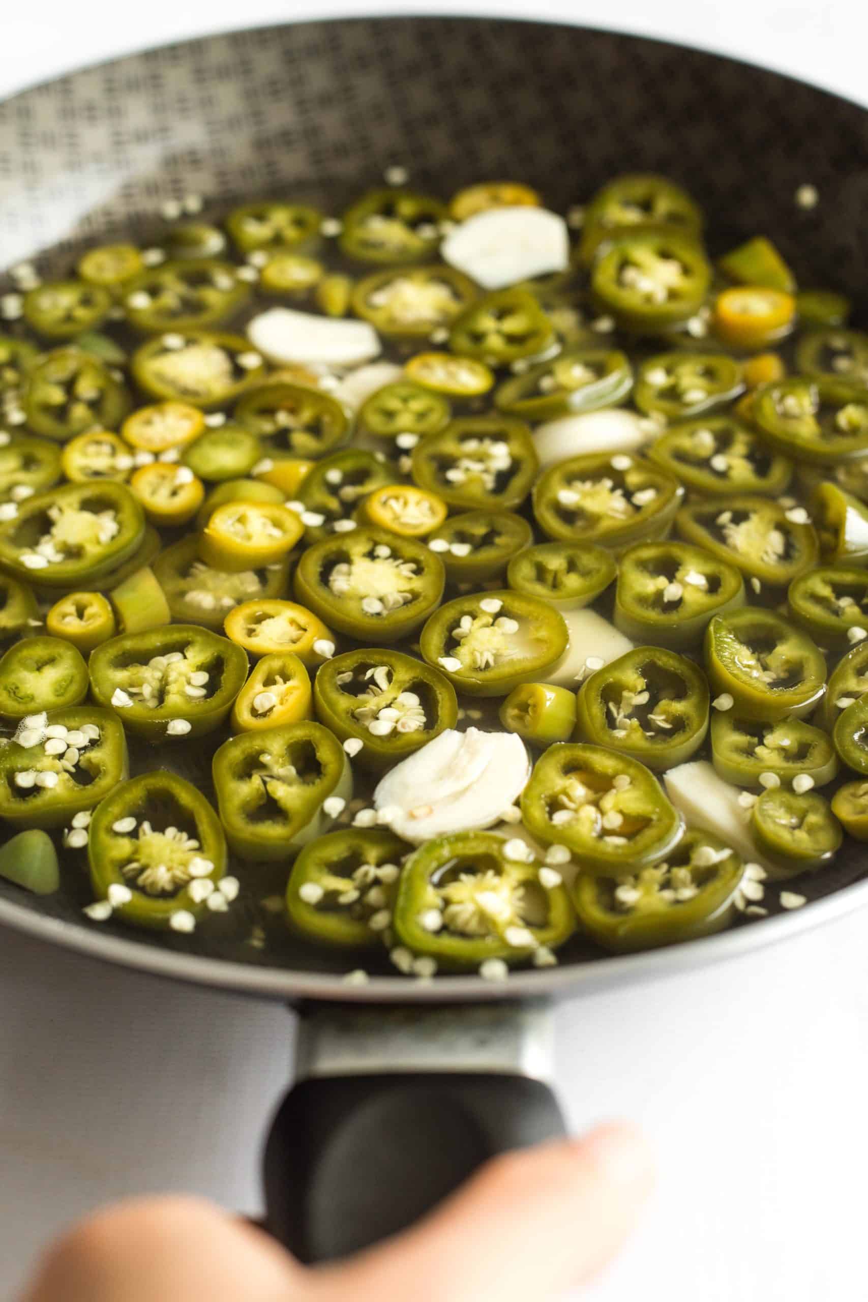 A large skillet of sliced jalapeño peppers in hot brine.