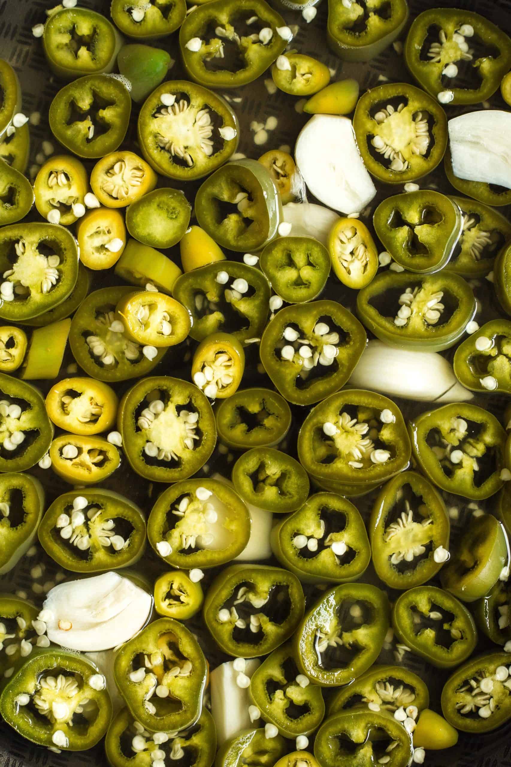 Up close shot of a skillet full of  jalapeño rings in a pickling liquid.