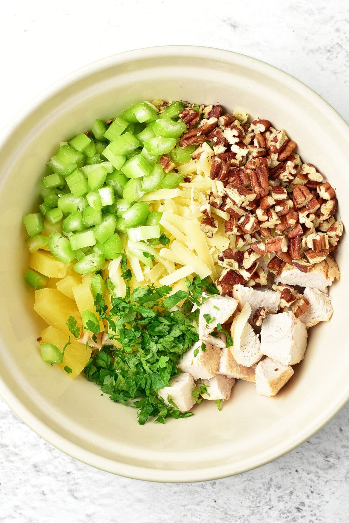A bowl of cubed chicken, chopped pecans, diced celery and pineapple.