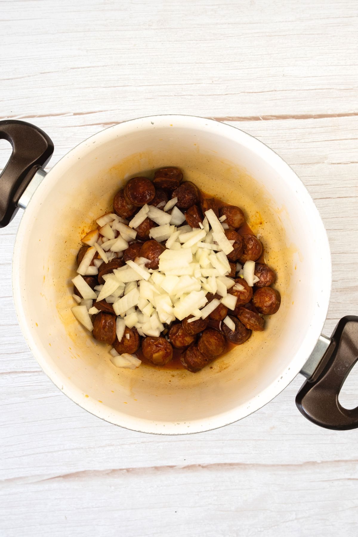 Sliced chorizo and diced onions in pot.