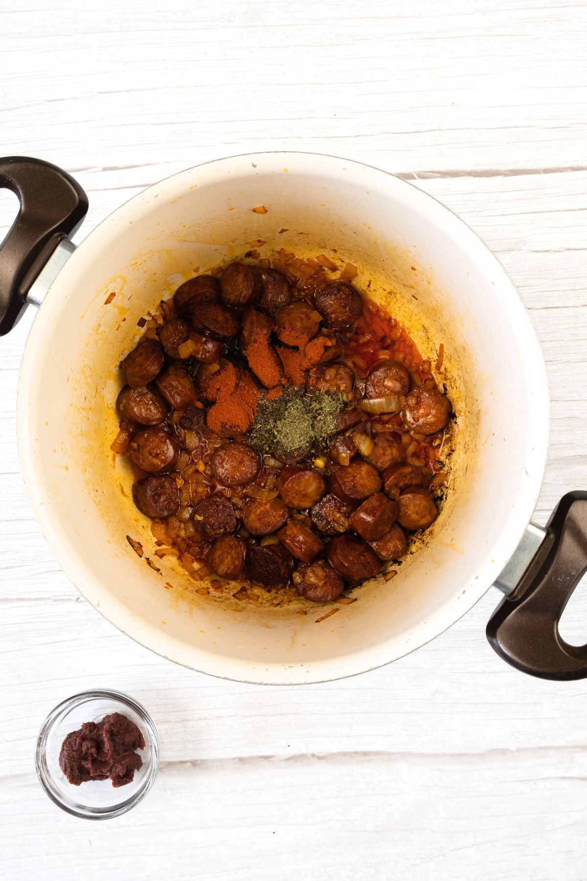 Sautéed chorizo slices and spices in pot.