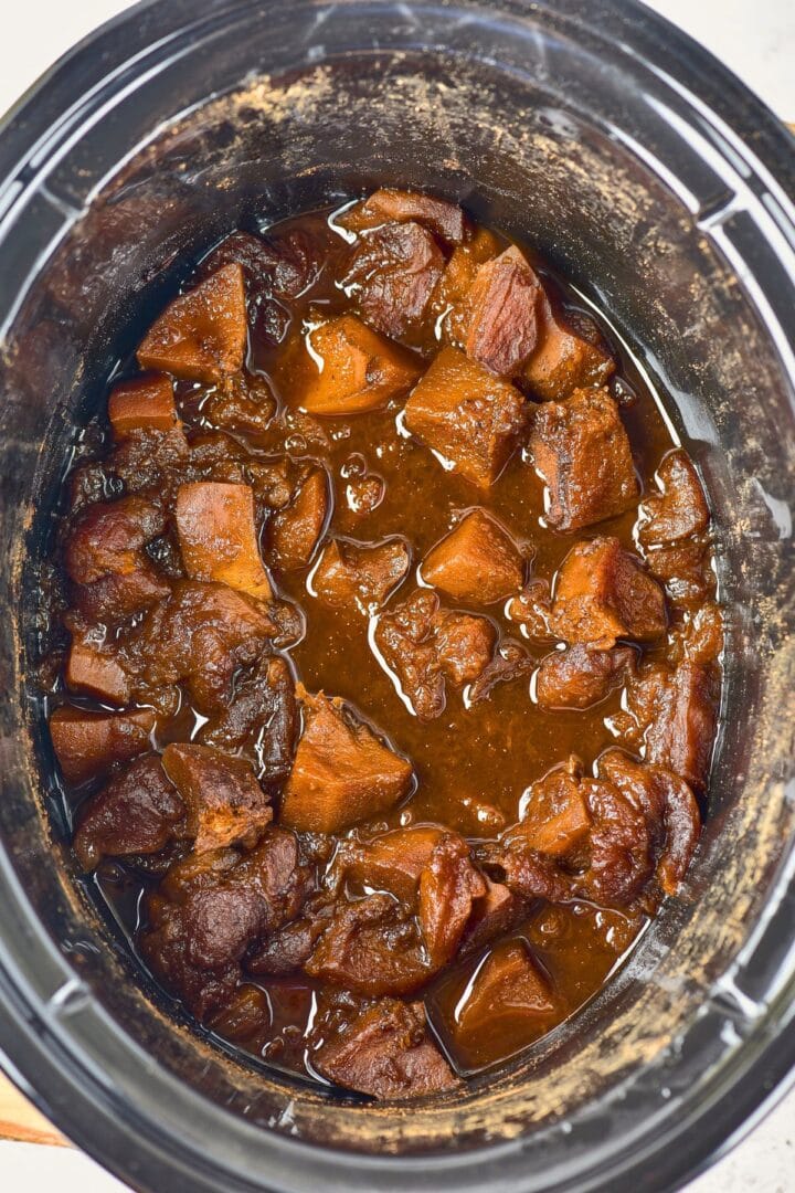 Cooked pumpkin and apples in brown juice in slow cooker.