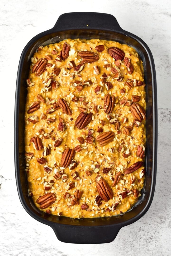 Pumpkin oatmeal mixture topped with pecans in baking dish.