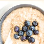 Top down view of a hand reaching for a bowl of porridge