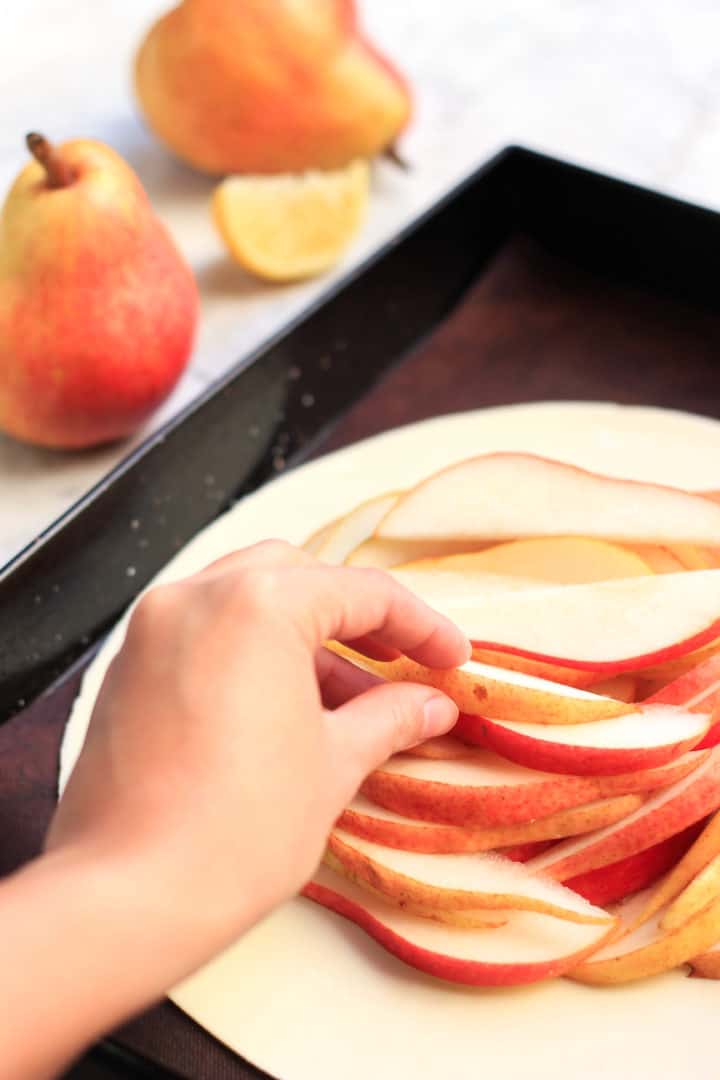 Hand arrange red pear slices on a pastry crust.