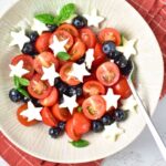 Cherry tomatoes, blueberries, mozzarella stars and basil leaves in bowl.