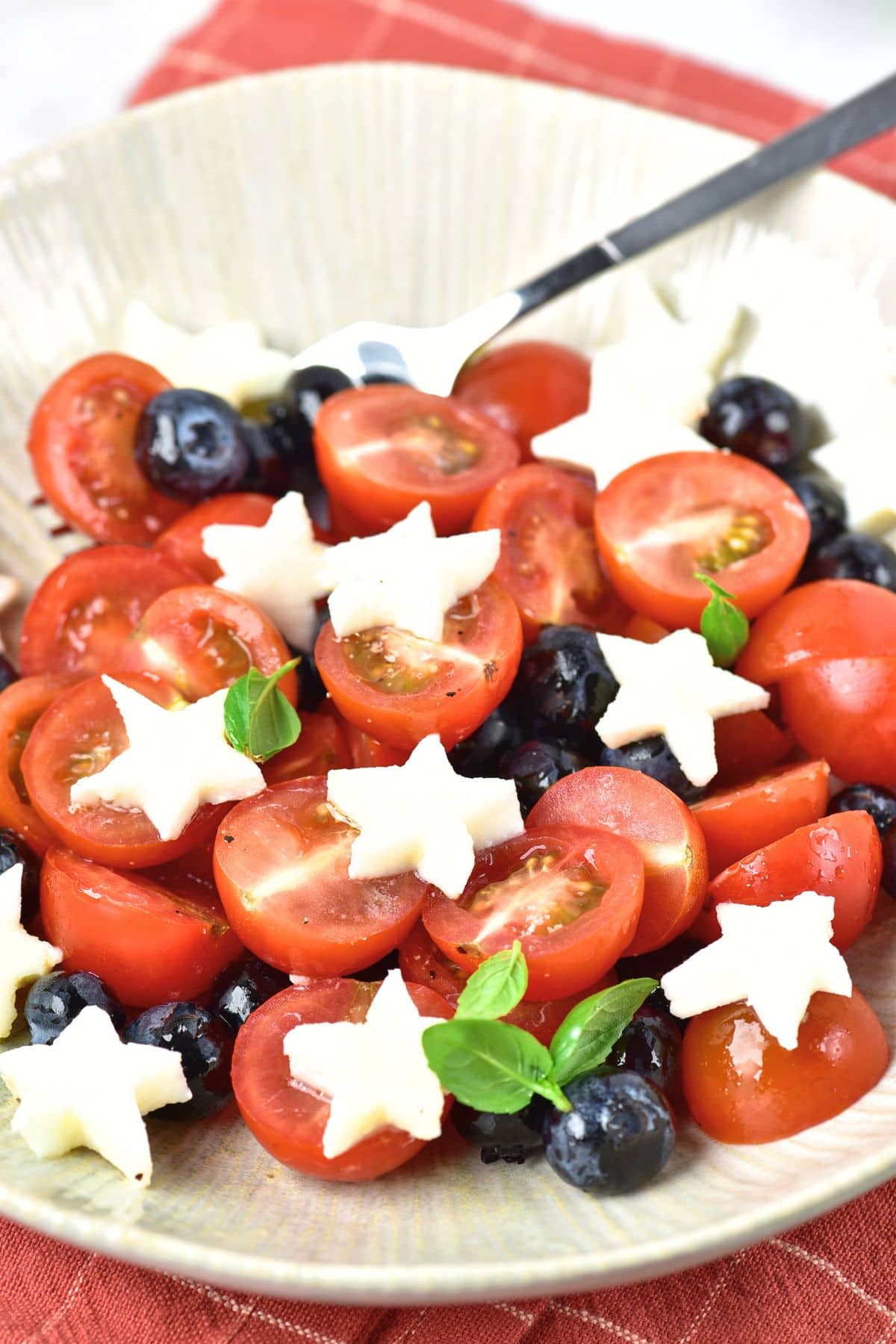 Up close view of star shaped mozzarella on top of cherry tomatoes and blueberries.