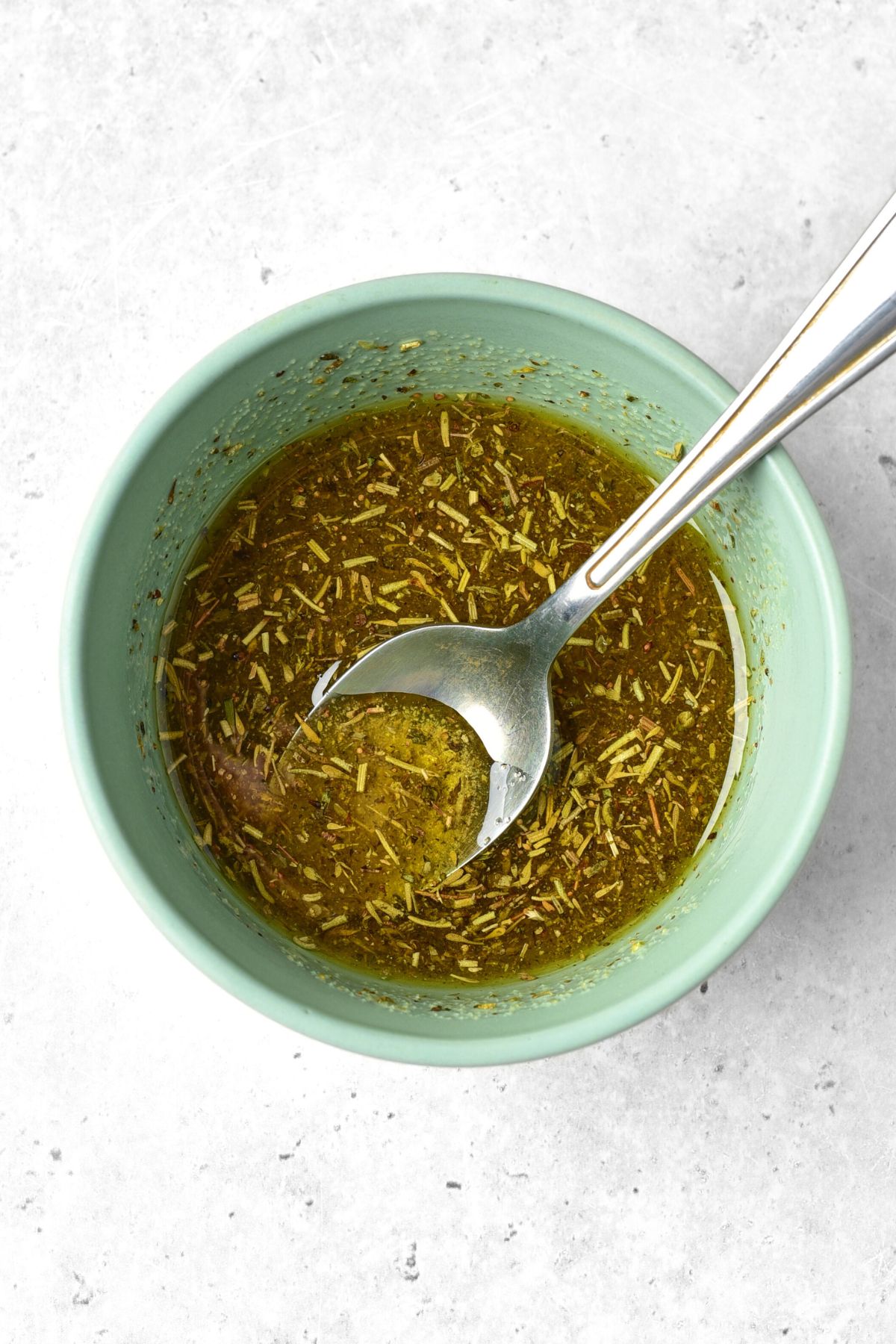 A green bowl with dried herbs in olive oil