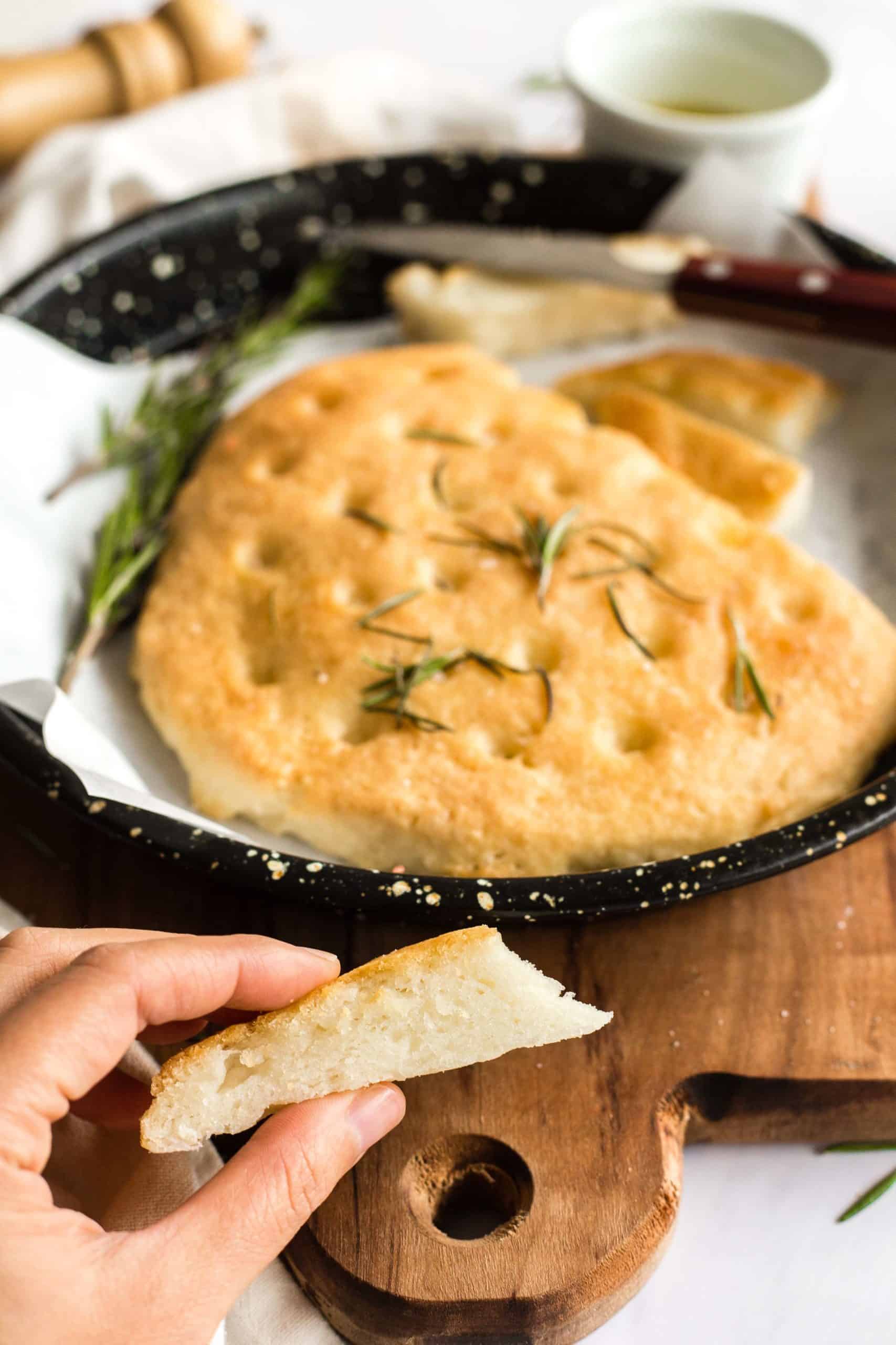 Hand holding a slice of gluten-free rosemary focaccia.
