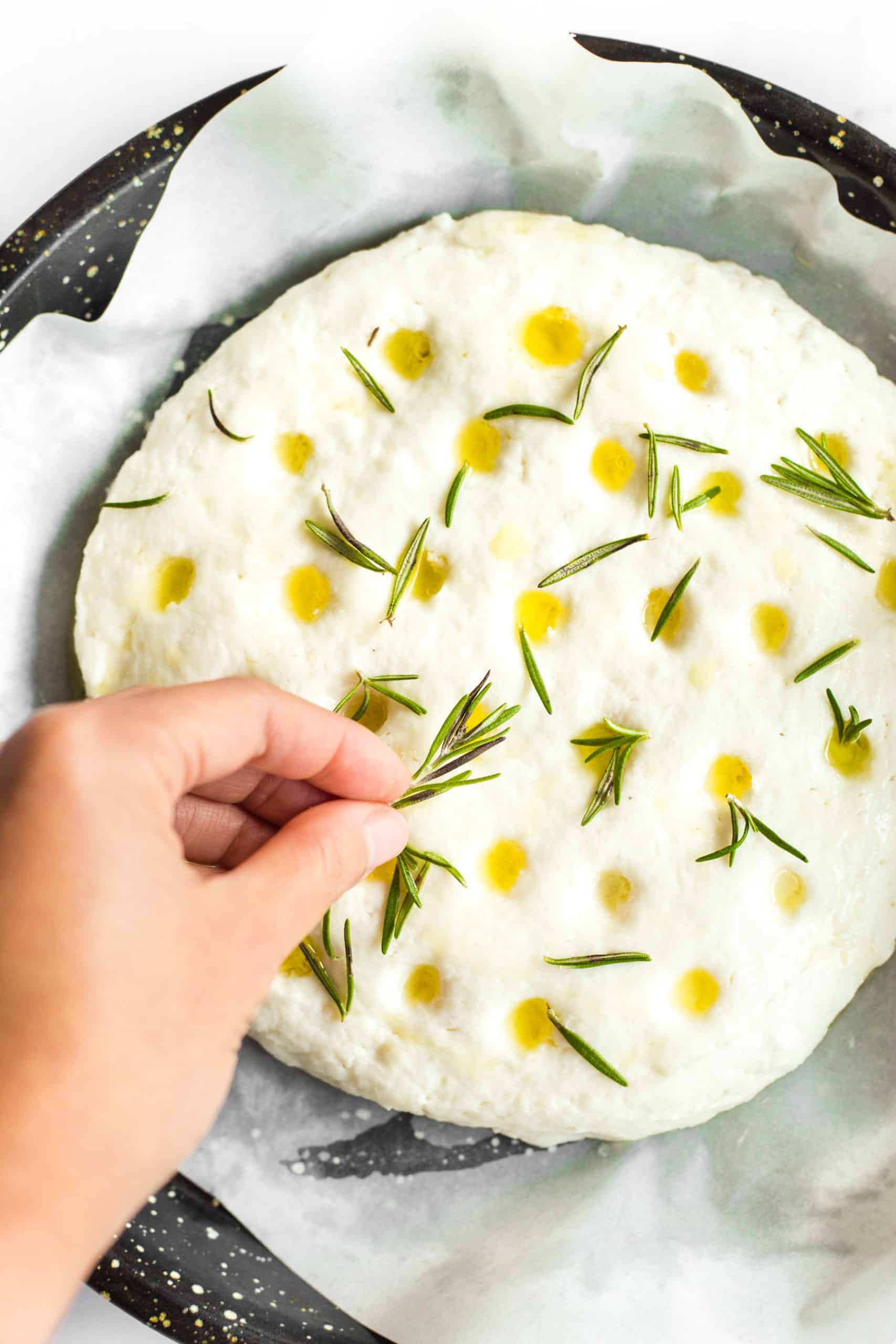 Sprinkling fresh rosemary leaves on top of gluten free focaccia dough.