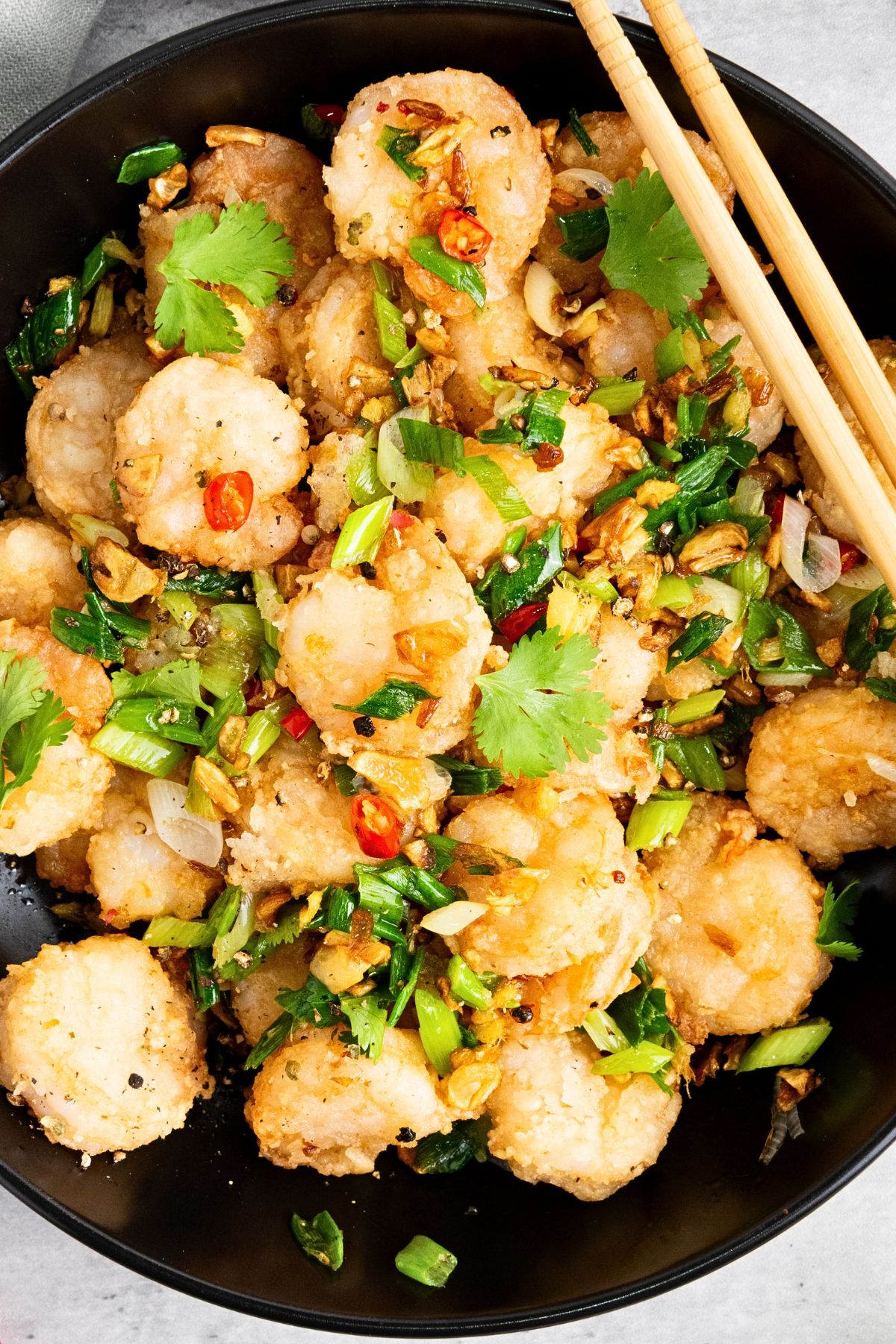 A bowl of salt and pepper shrimp garnished with scallions and cilantro
