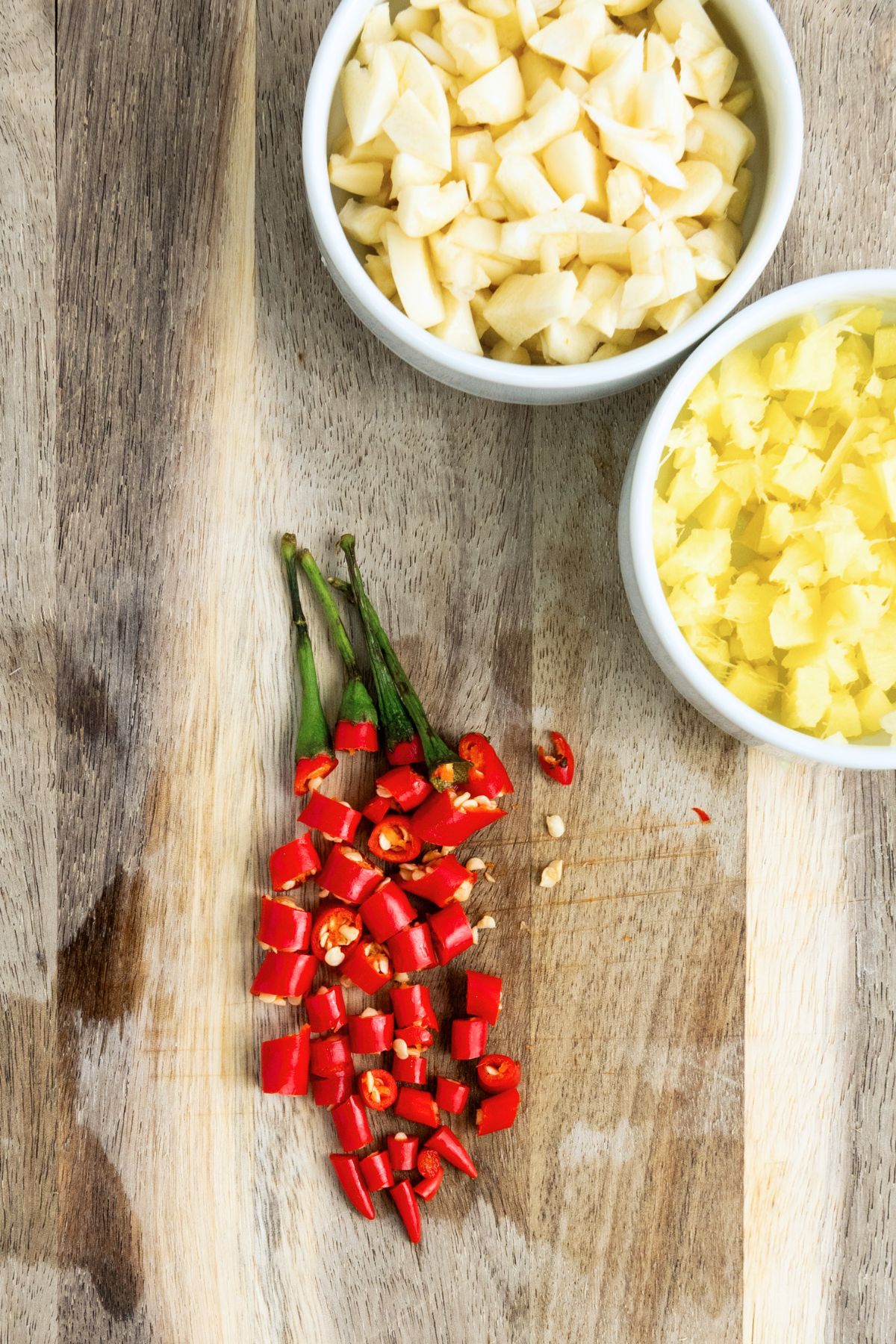 Chopped chili, garlic and ginger in bowls on a wooden board.