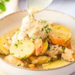 Spoon drizzling creamy sauce over slow cooker chicken and potatoes