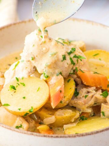 Spoon drizzling creamy sauce over slow cooker chicken and potatoes