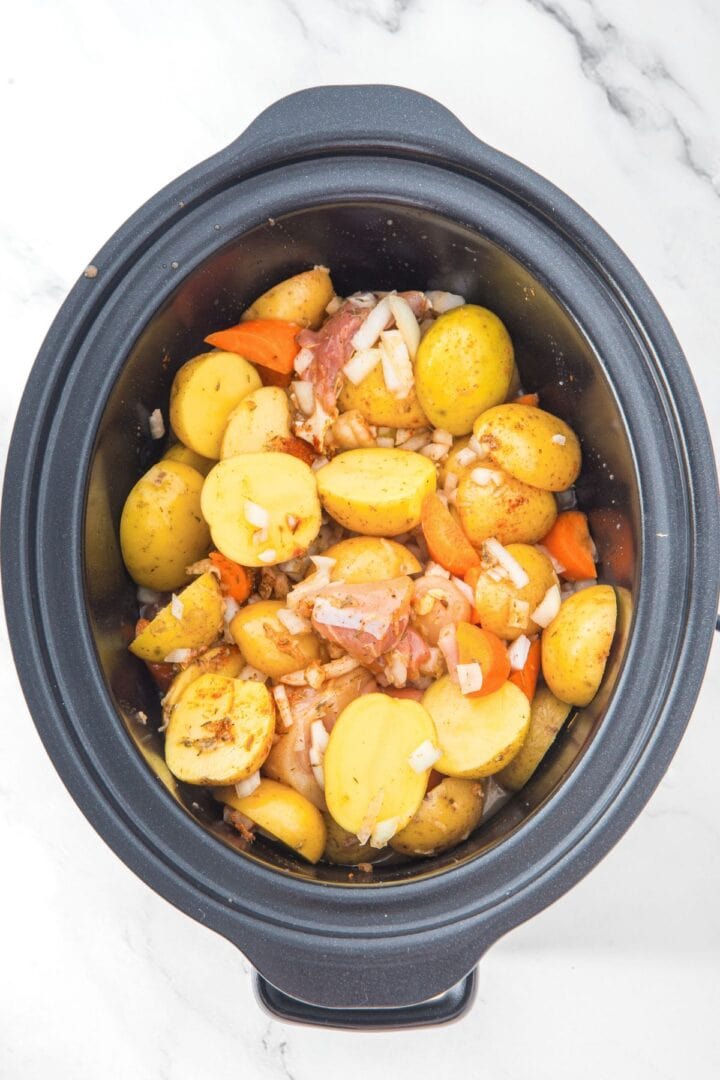 Top down view o raw chicken, potatoes, carrots and onions in slow cooker