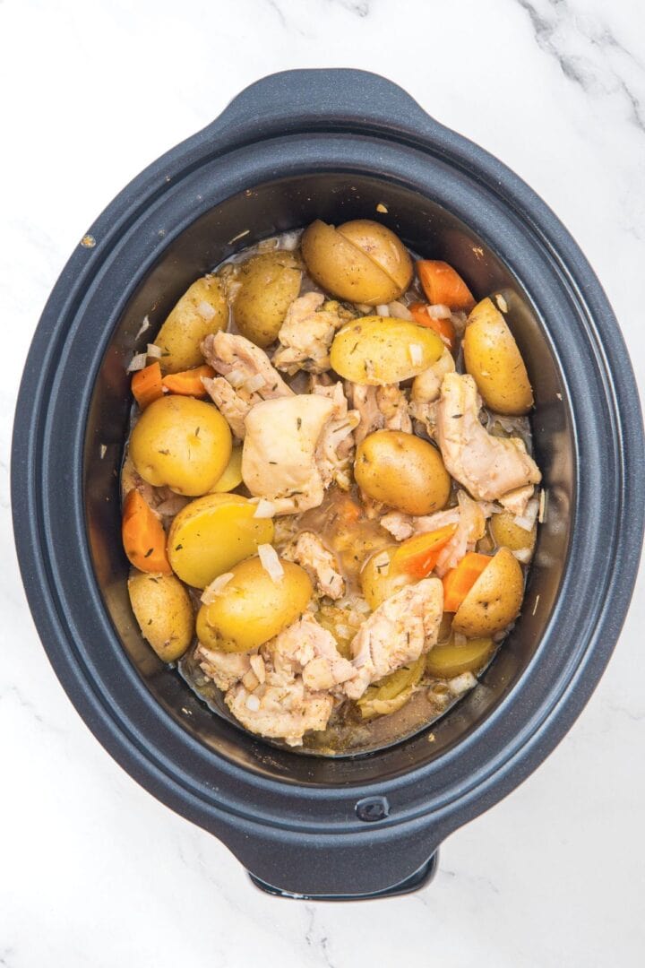 Partially cooked chicken and potatoes in slow cooker bowl.