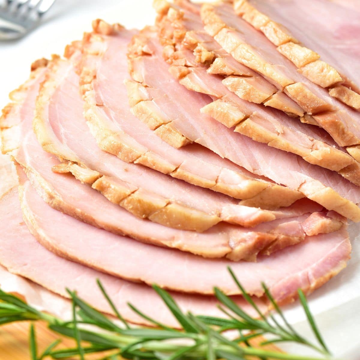 Up close view of sliced ham and fresh rosemary sprig