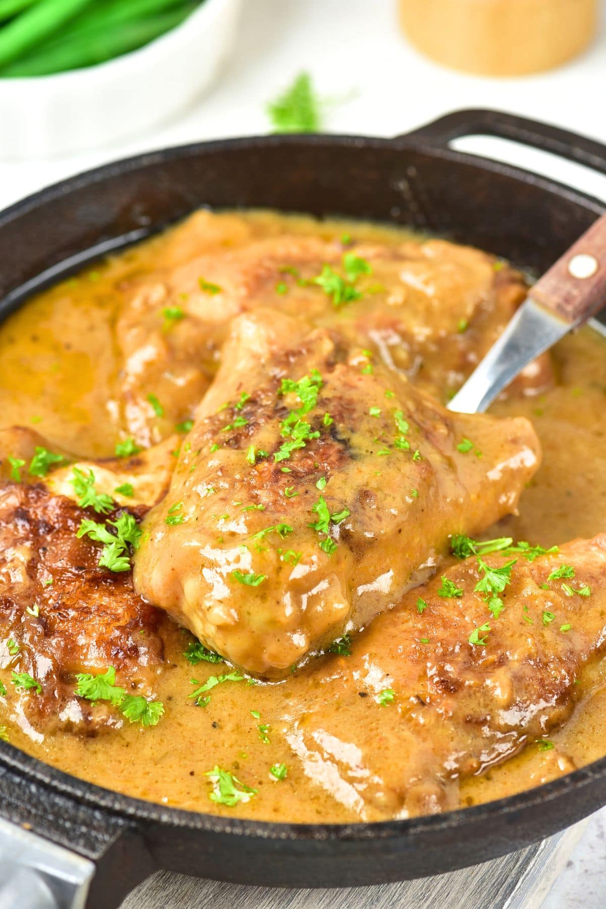 Smothered Chicken Thighs (Gluten-Free, Dairy-Free) Holding up a spoonful of smothered chicken thighs in onion gravy from skillet