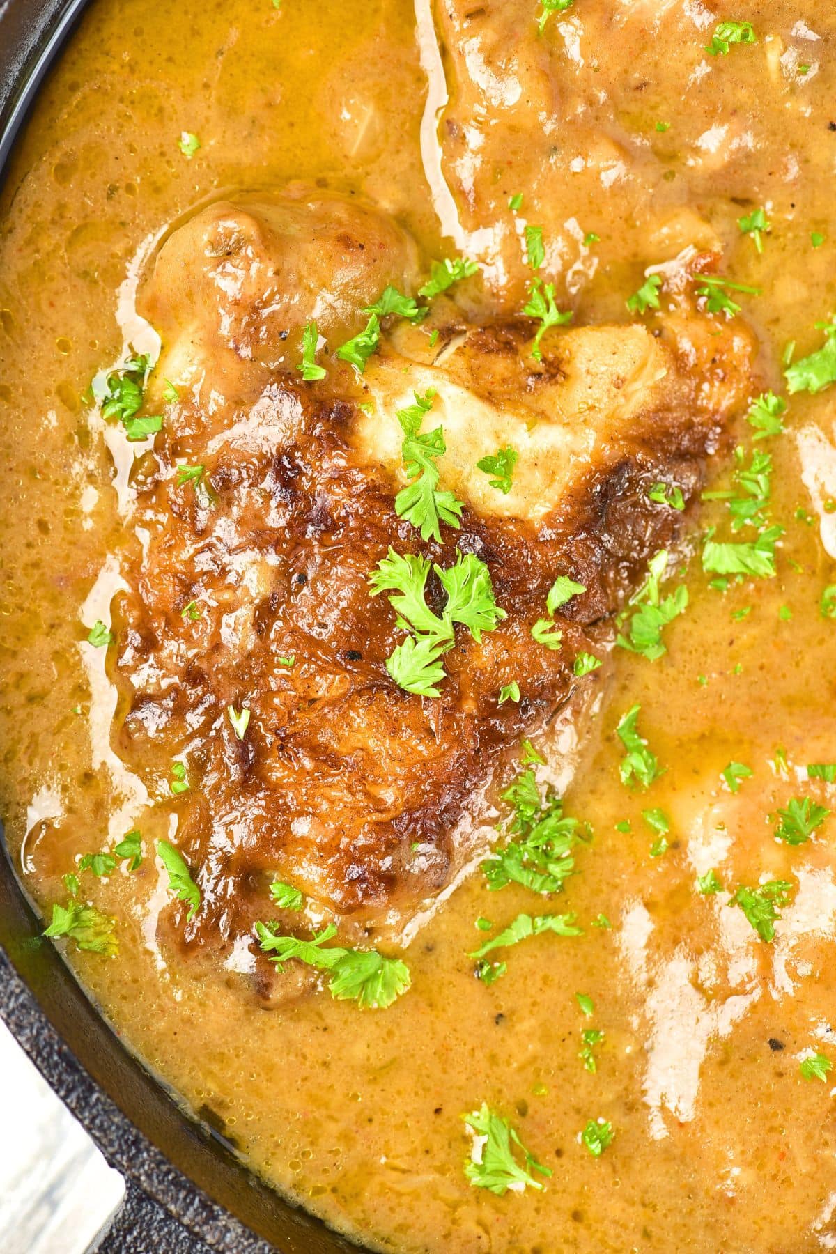 Southern Smothered Chicken and Gravy Up close view of a skillet with smothered chicken and gravy sprinkled with chopped parsley.