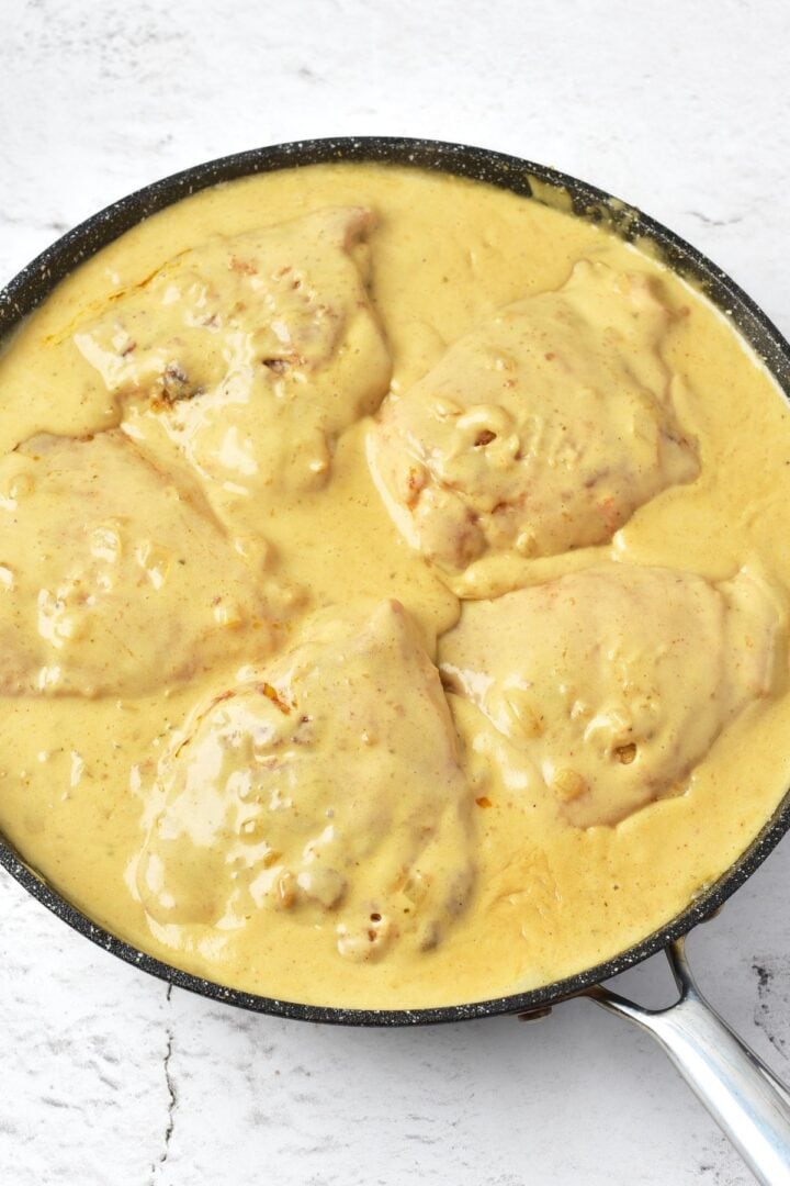 Chicken thighs in pale yellow mixture in skillet