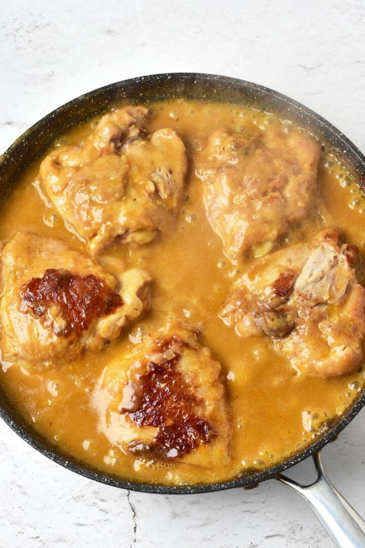 Cooked chicken thighs in brown gravy mixture in skillet