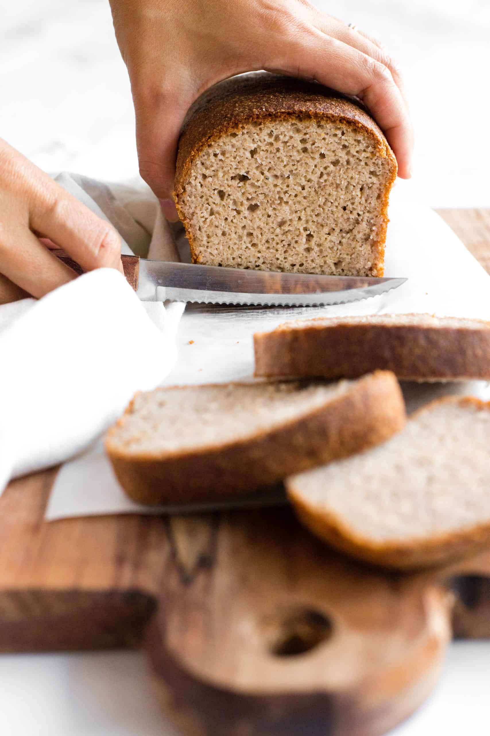 Hand slicing into a loaf of gluten-free rice bread.