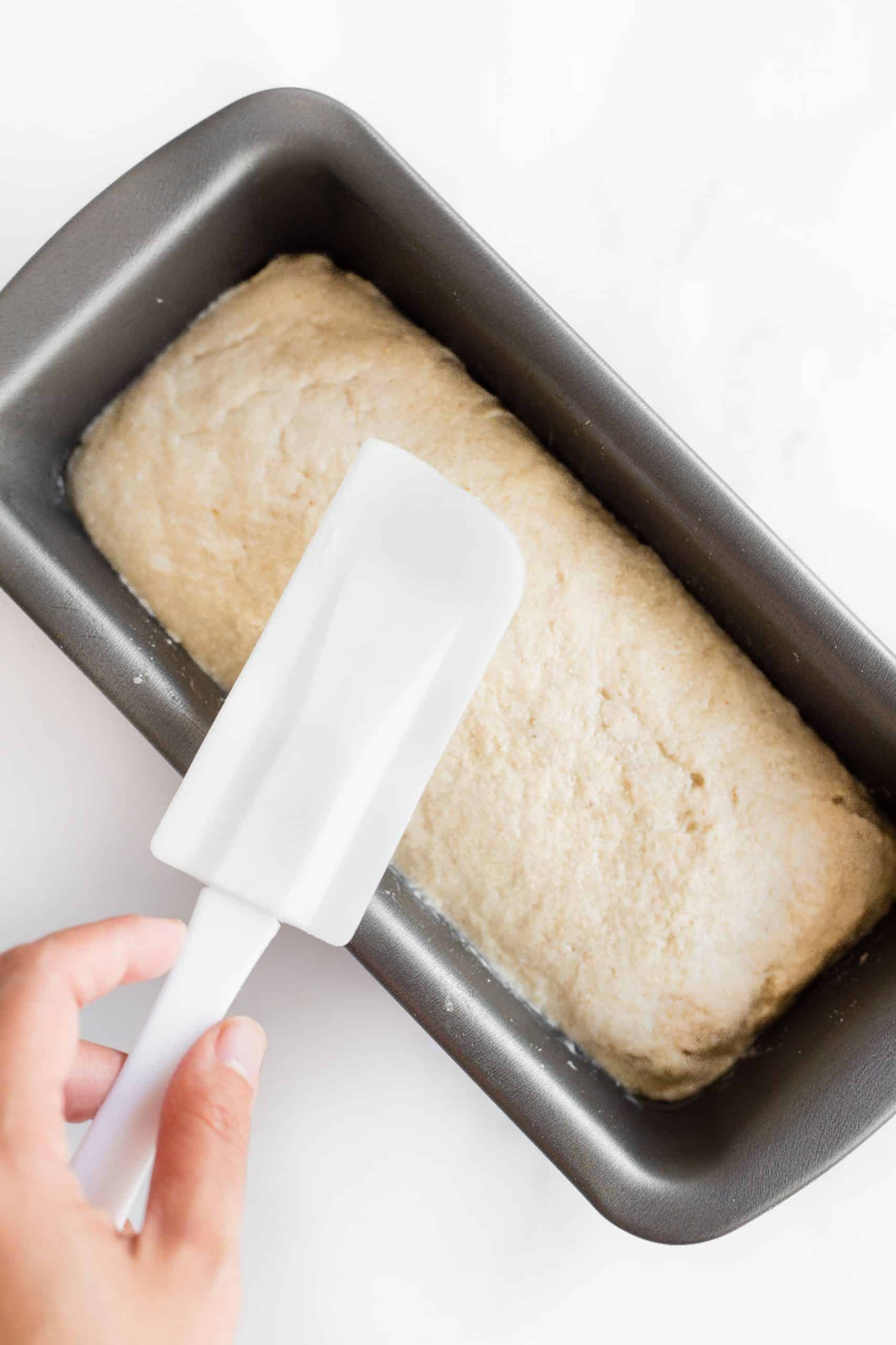 Using a spatula to smooth out the top of bread dough in a pan.