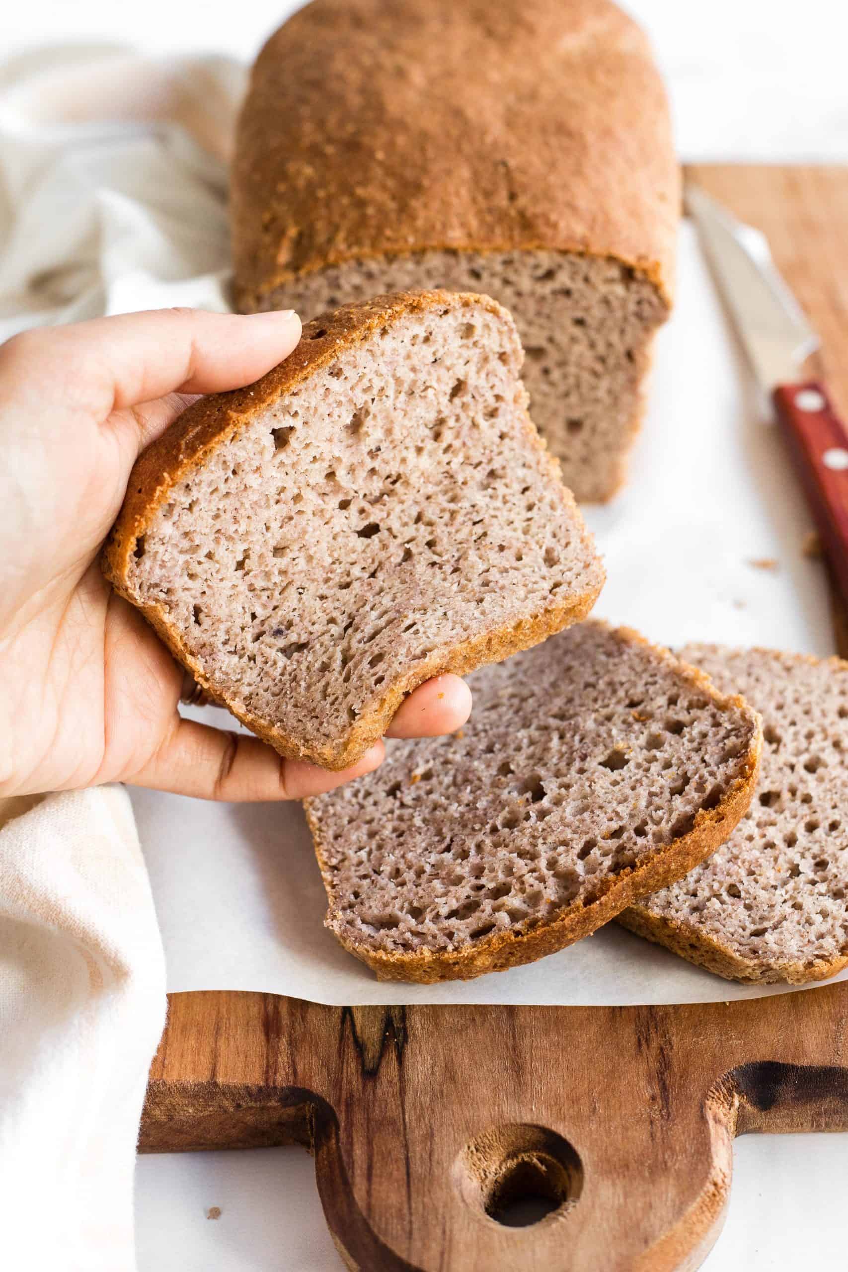 Hand squishing a slice of gluten-free brown bread.