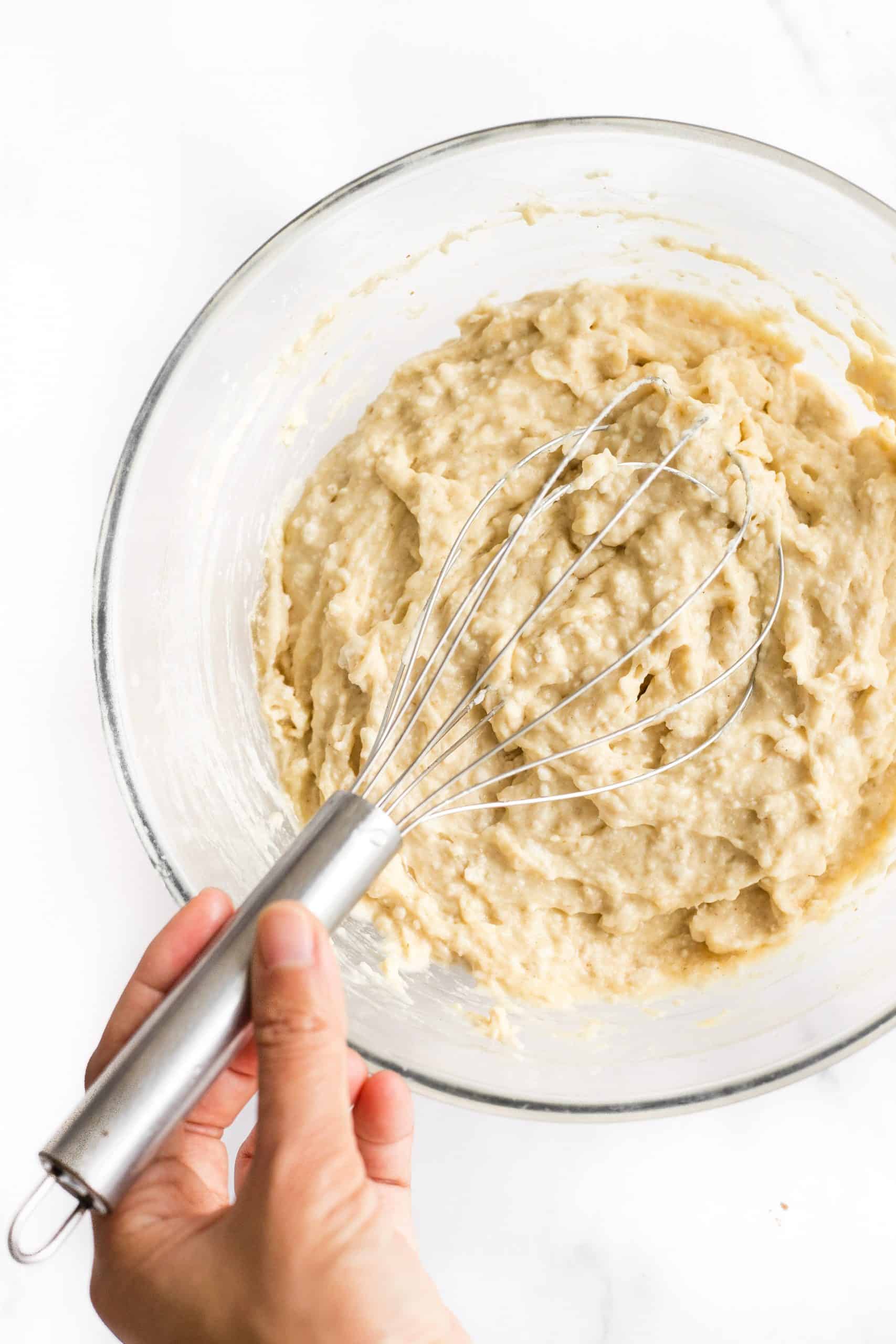 Using a whisk to mix dough in a glass bowl.